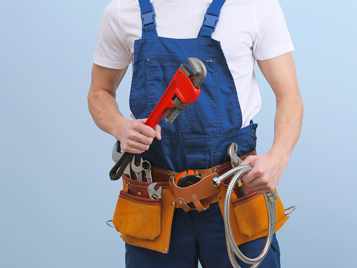 andsome young plumber with tools on color background.