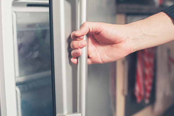 The hand of a young man is opening a freezer door.