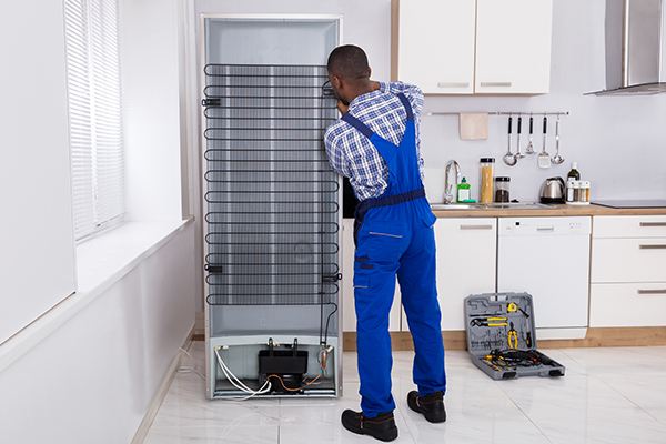 Refrigerator repairman working on the back of a fridge.