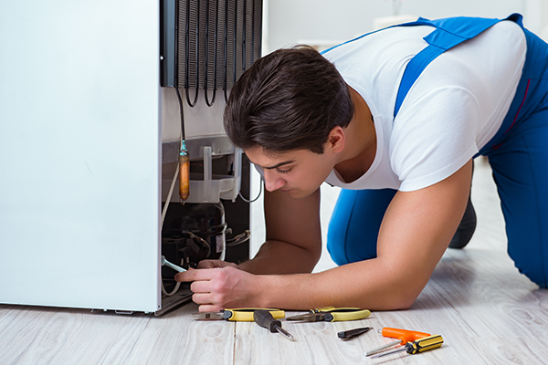 Refrigerator repairman looking under a fridge.
