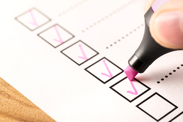 Person’s hand crossing off checkboxes with a pink highlighter.