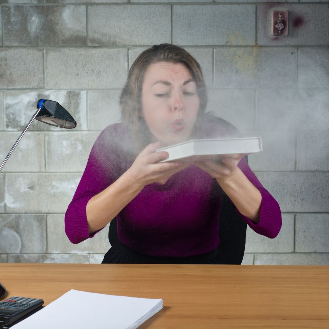 person blowing dust off a book