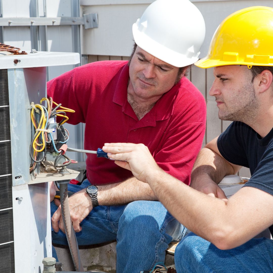 two HVAC workers repairing AC condenser
