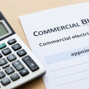 A commercial electric utility bill rests on a wooden desk next to a silver calculator.