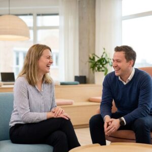 Two colleagues laugh together in a comfortable, brightly lit office environment.