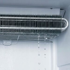 A close-up view of water dripping continuously from a compromised evaporator coil inside a cooler.