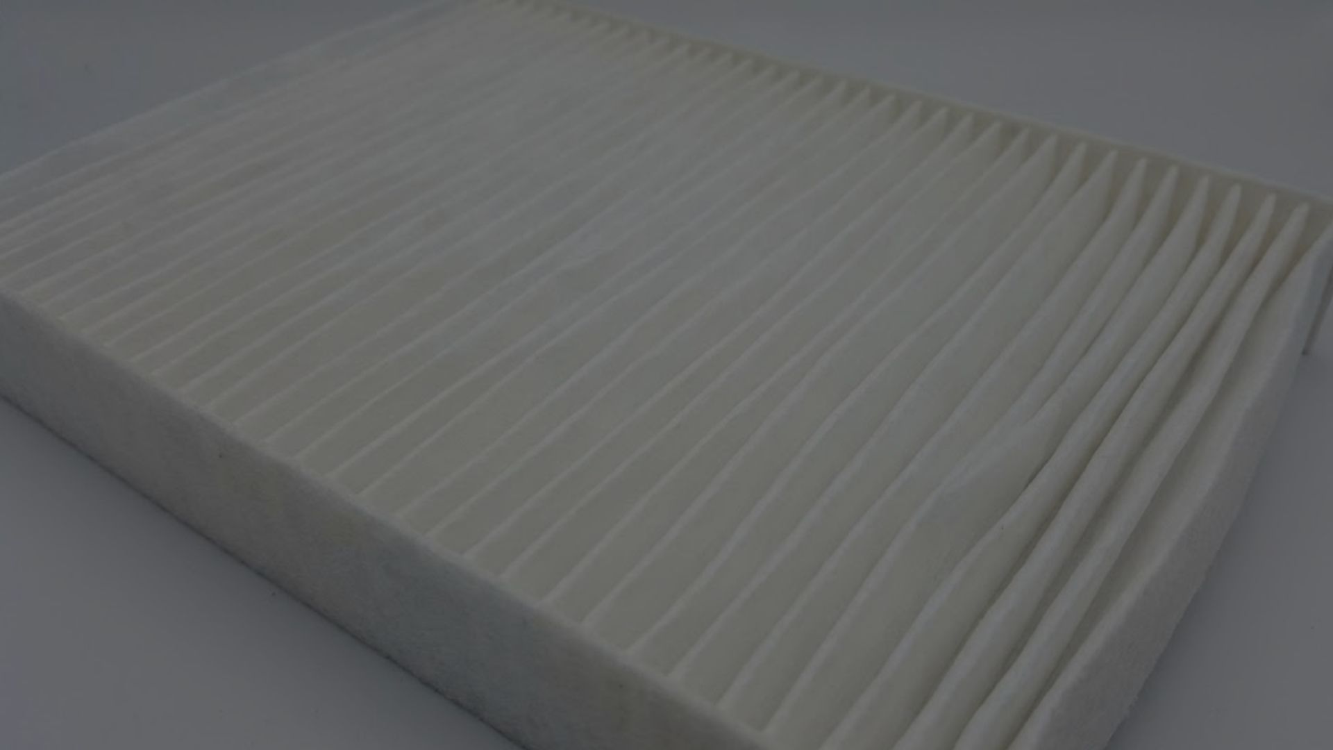 A close-up view of a standard, clean white air filter with light catching the fibers.